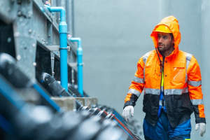 An engineer working in the pouring rain, wearing a reflective orange coat.