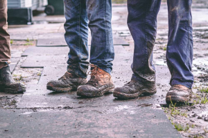 Three men with muddy work boots, outside in wet weather.