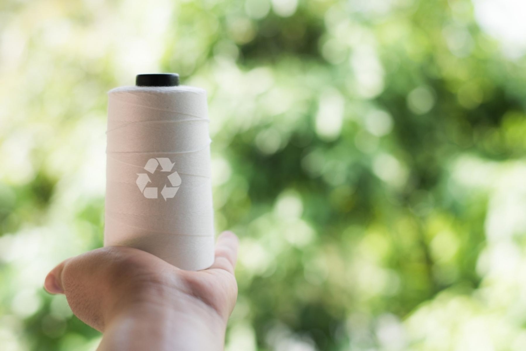 Hand holding white yarn with the recycling symbol on top