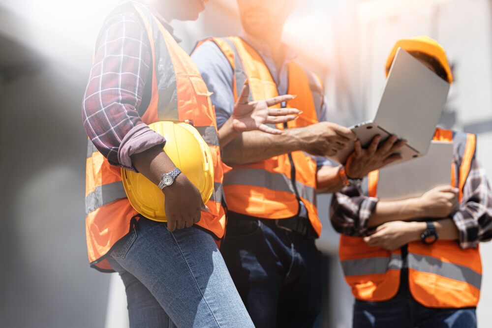 Three experts dressed in casual workwear for men. They inspect a commercial building construction site. 