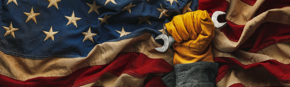 A worn and heavy-duty work glove-covered hand grips a wrench before an American flag.